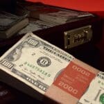 $2000 in $100 dollar bills in a stack sitting in front of an open briefcase filled with more stacks of money.