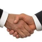 Close-up of two hands in a hand shake. Cuffs of white shirt under black jackets visible.