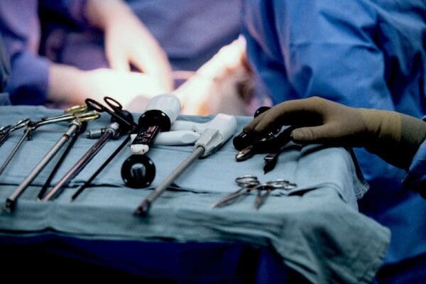 Close-up of surgical instruments on a tray. Blurred image of two surgeons' gloved hands at work in the background.